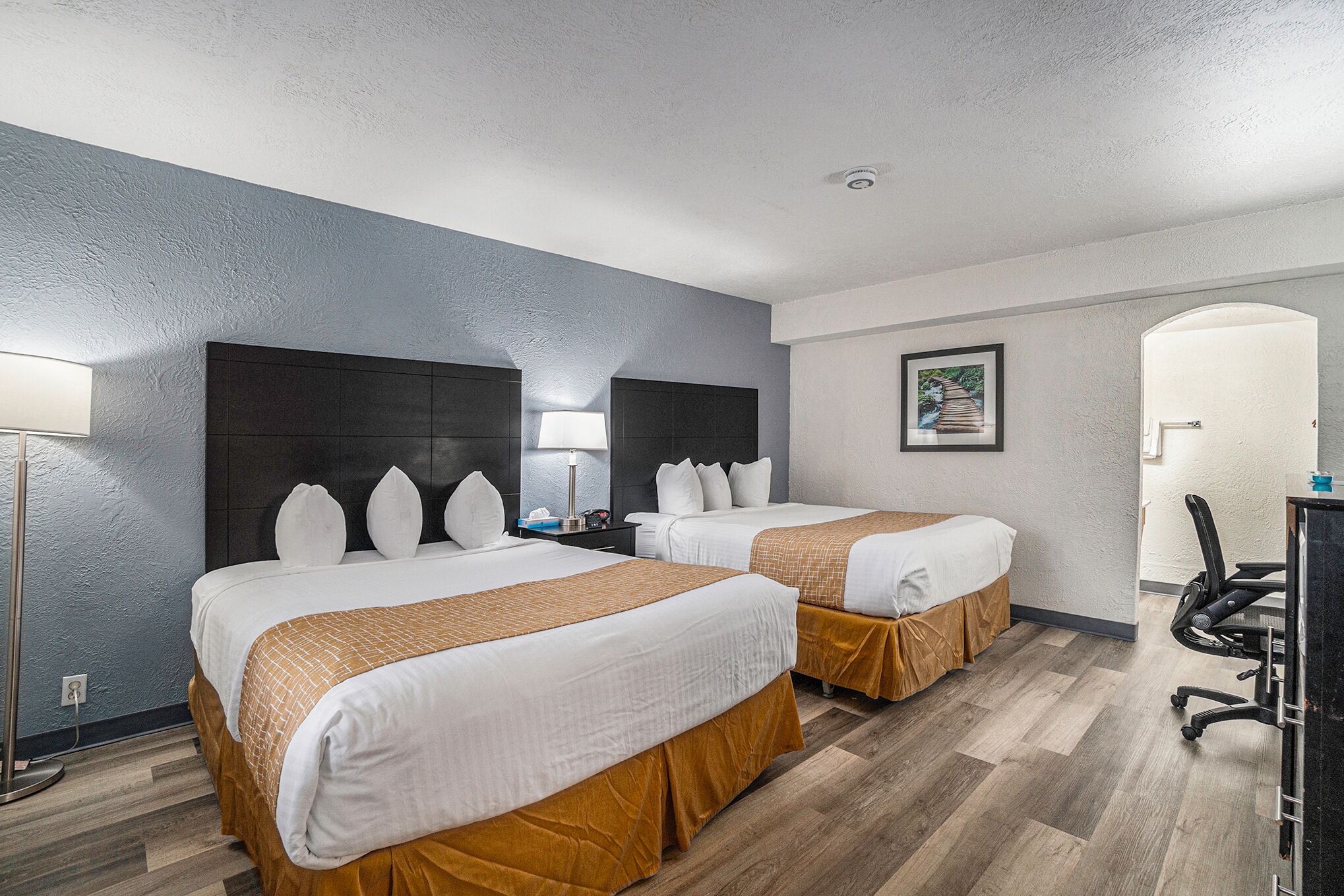 Een hotelkamer met twee bedden, een bureau, een stoel, een lamp en een foto aan de muur.