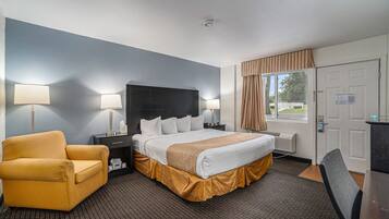 Ein Hotelzimmer mit Bett, Sessel, Schreibtisch und einem Fenster mit Vorhängen.