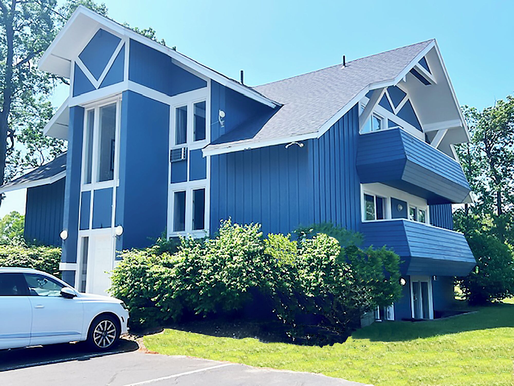 A modern two-story house with a blue exterior and white trim, featuring large windows and a garage.