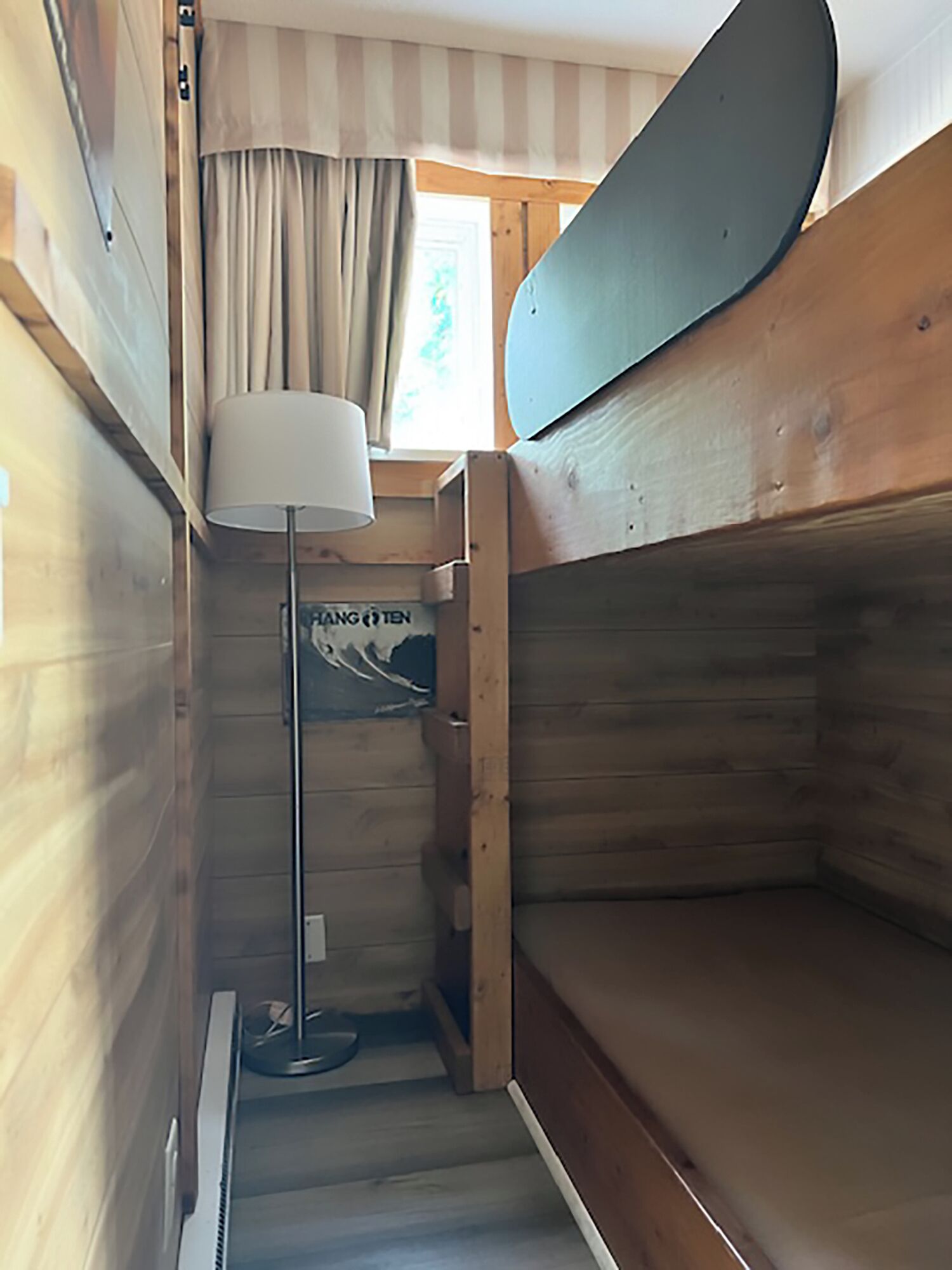 A narrow, wooden interior with bunk beds, a floor lamp, and a poster on the wall.