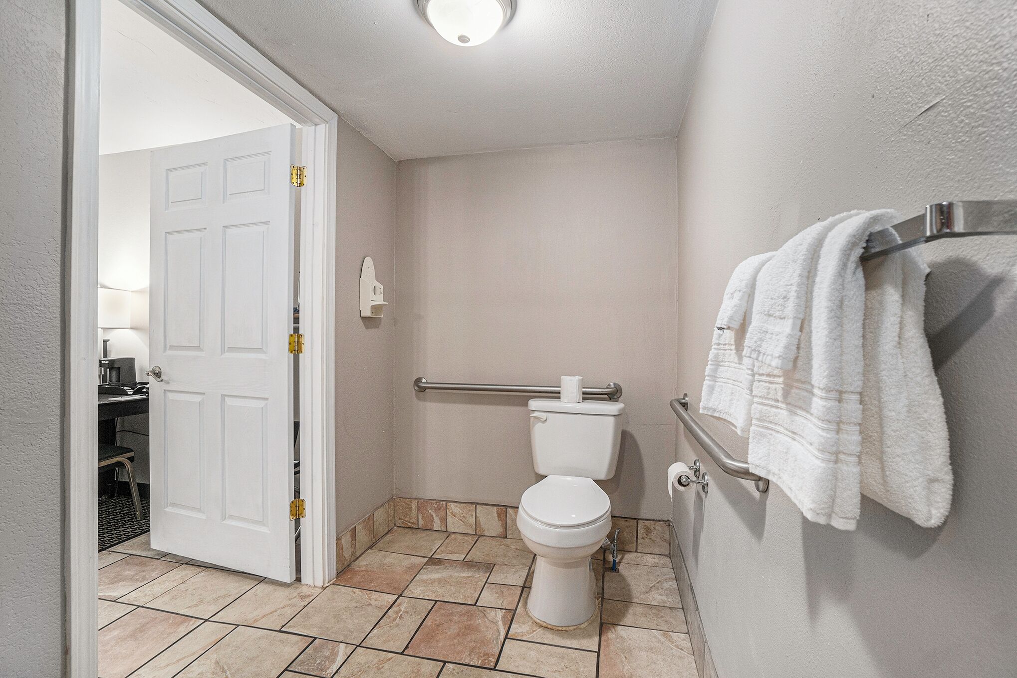 Une salle de bain équipée de toilettes, d’une barre d’appui et d’un porte-serviettes.