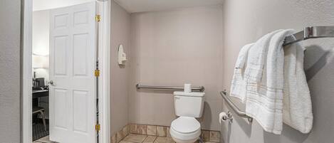 Une salle de bain équipée de toilettes, d’une barre d’appui et d’un porte-serviettes.