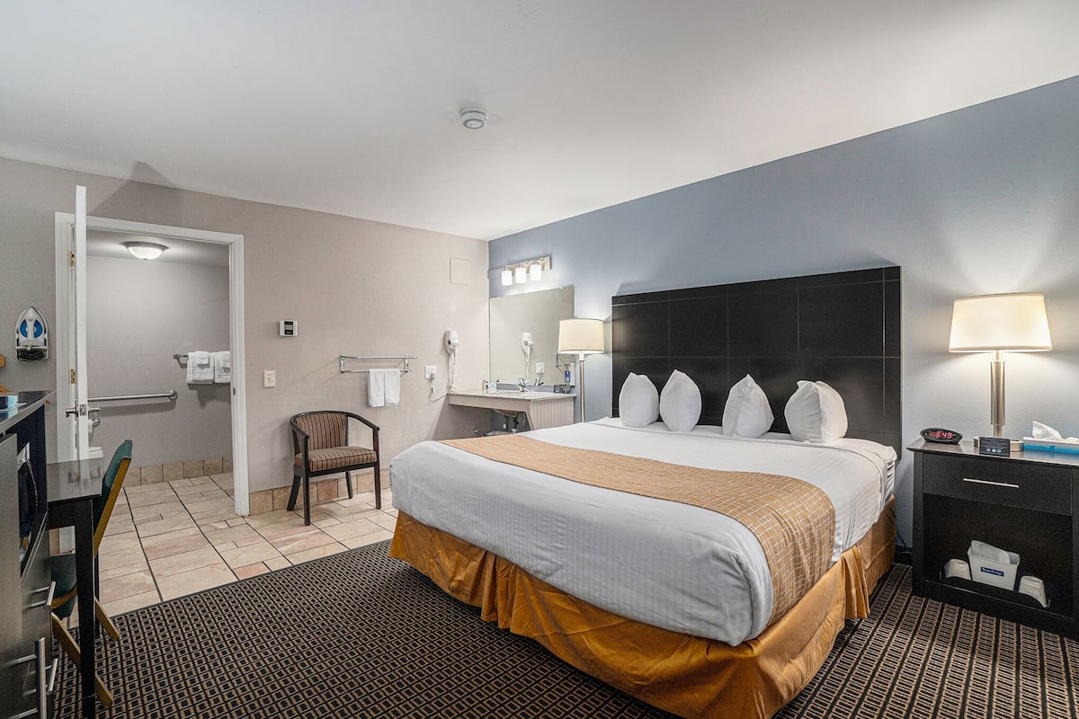 Une chambre d’hôtel avec un grand lit, un bureau, une chaise, une salle de bain et une table de chevet avec une lampe.