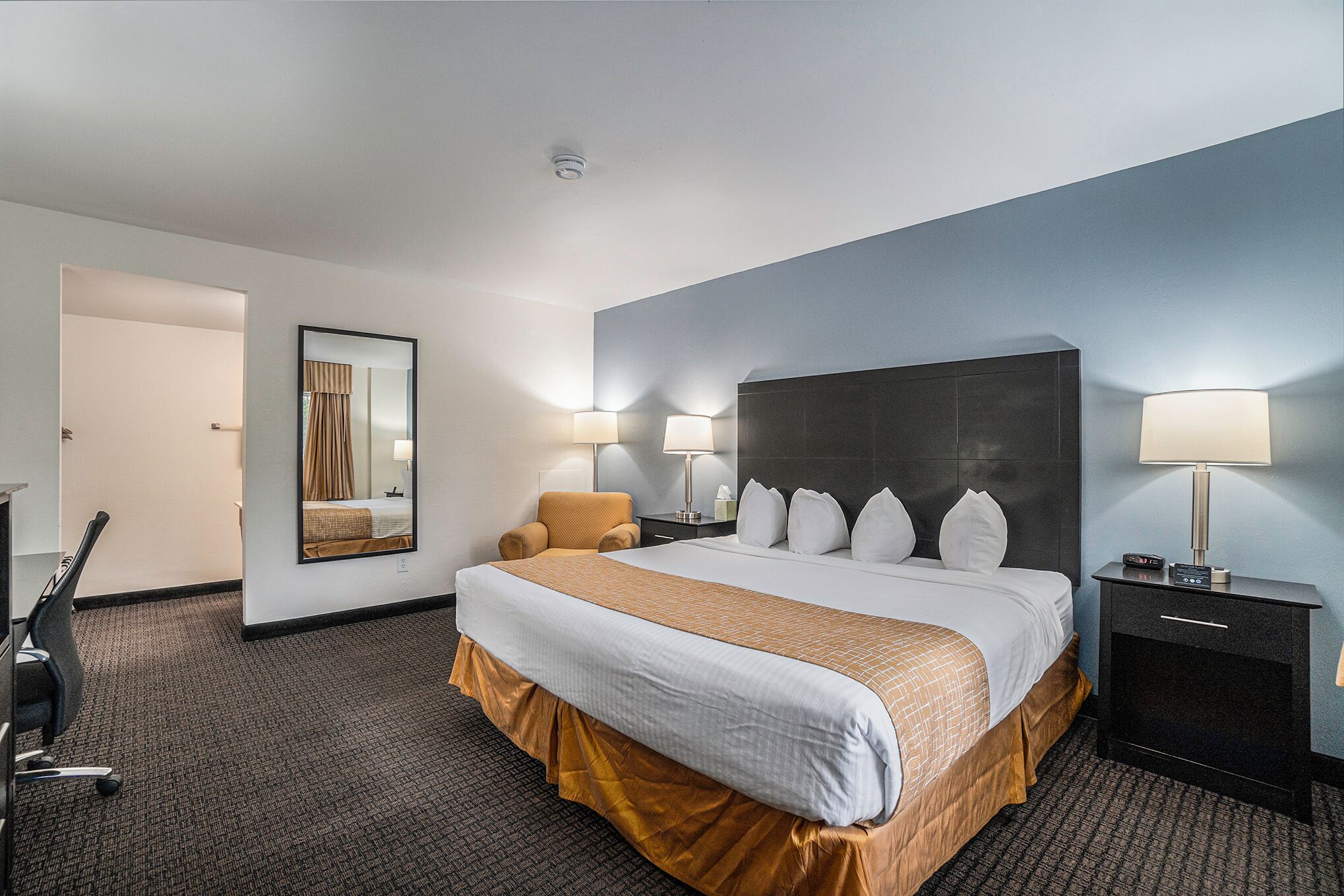 A hotel room with a large bed, two bedside lamps, a chair, a desk, and a mirror.