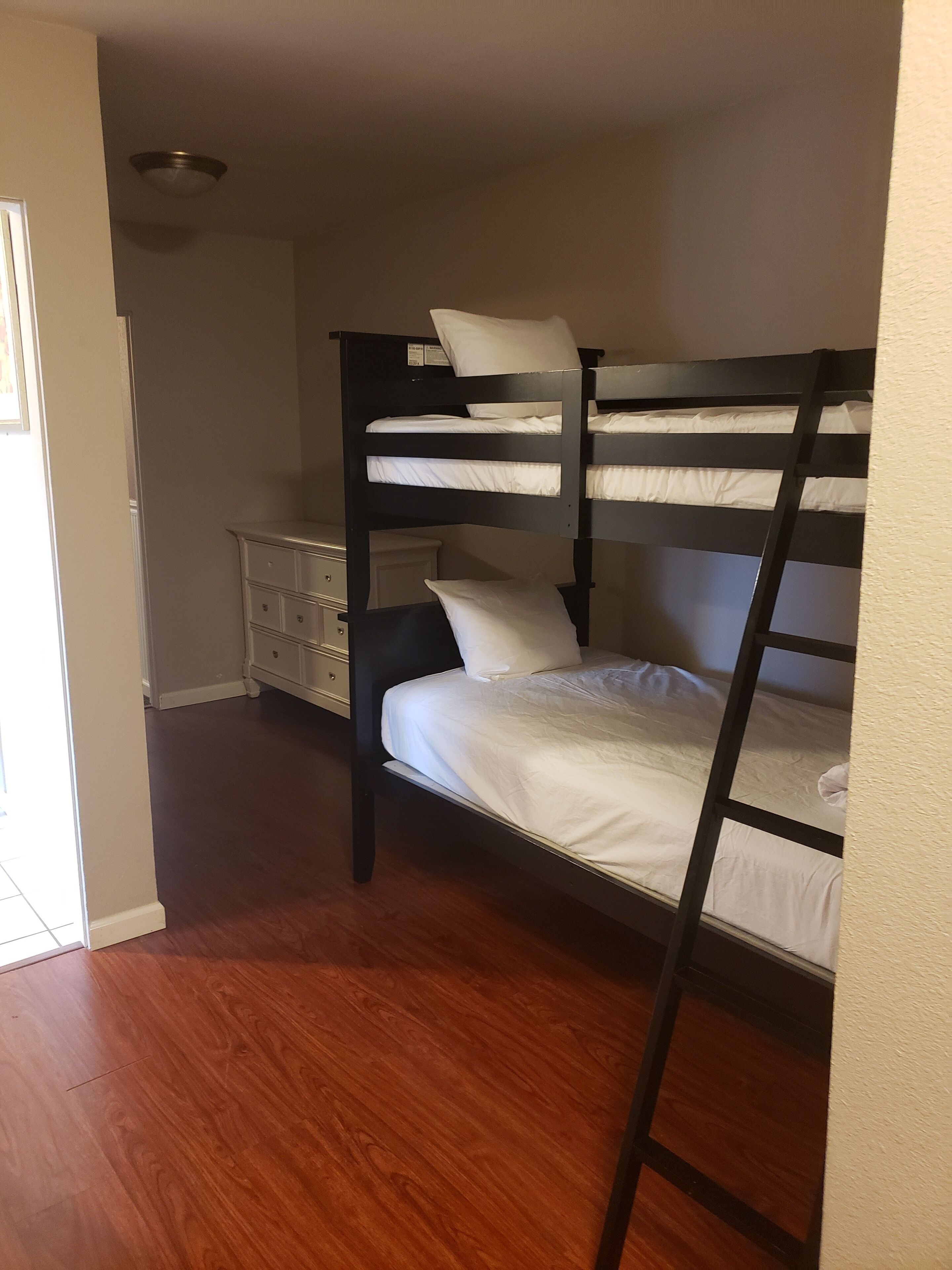 Una cama litera con ropa de cama blanca, un aparador y piso de madera.