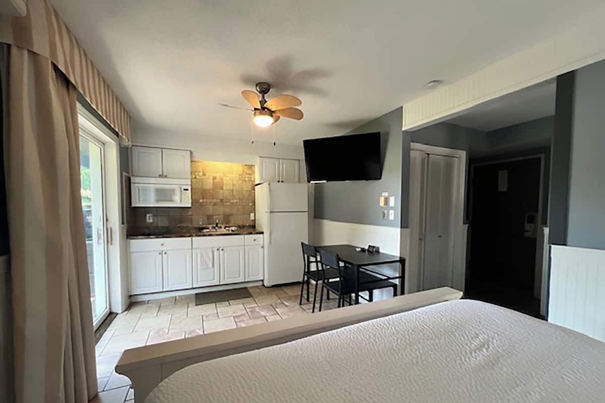 Une chambre d’hôtel comprenant un lit, un ventilateur de plafond, une kitchenette équipée d’un four à micro-ondes et d’un réfrigérateur, une table à manger avec des chaises et un téléviseur fixé au mur.