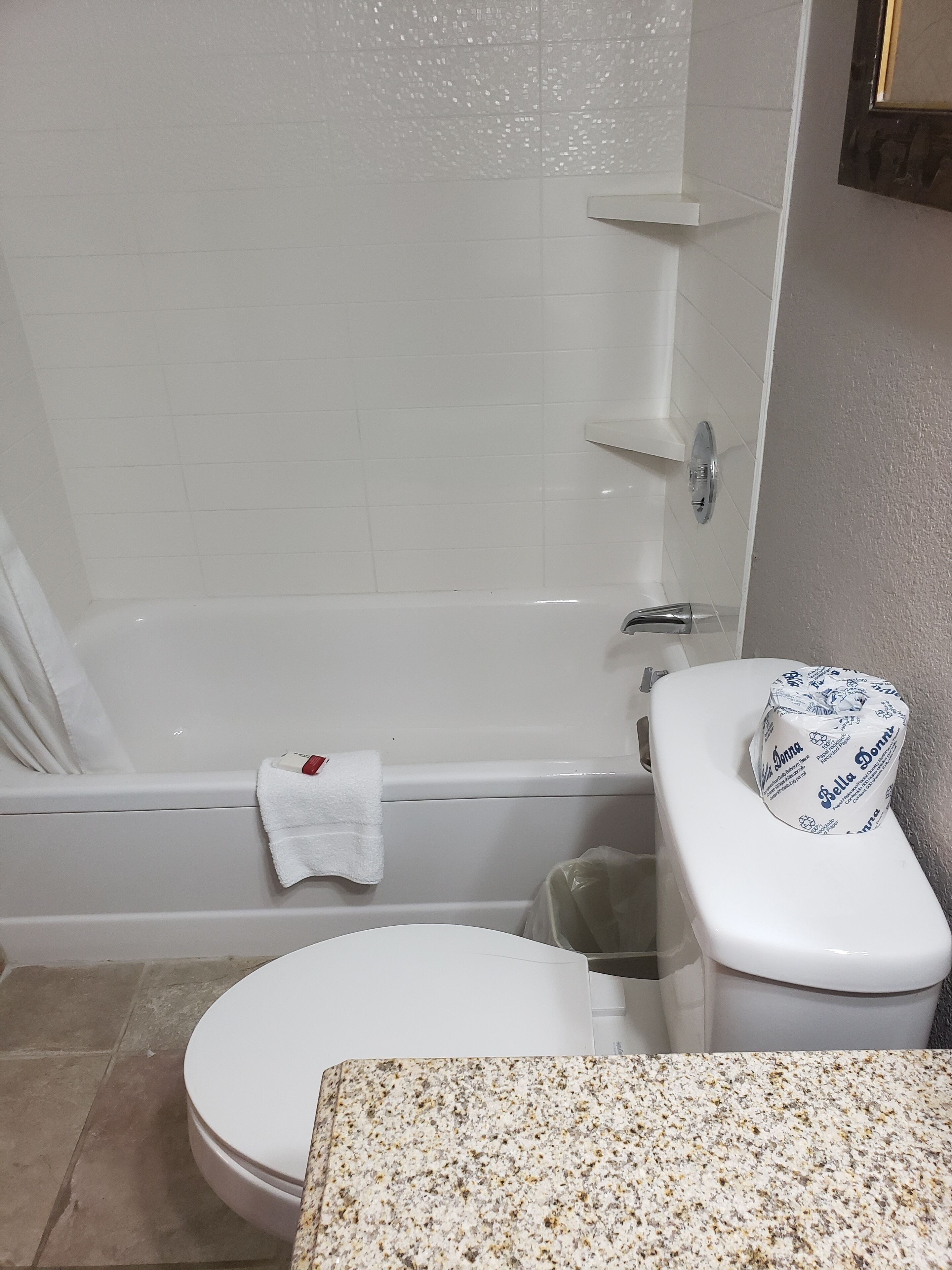 A bathroom with a white bathtub, a toilet, and a granite countertop.