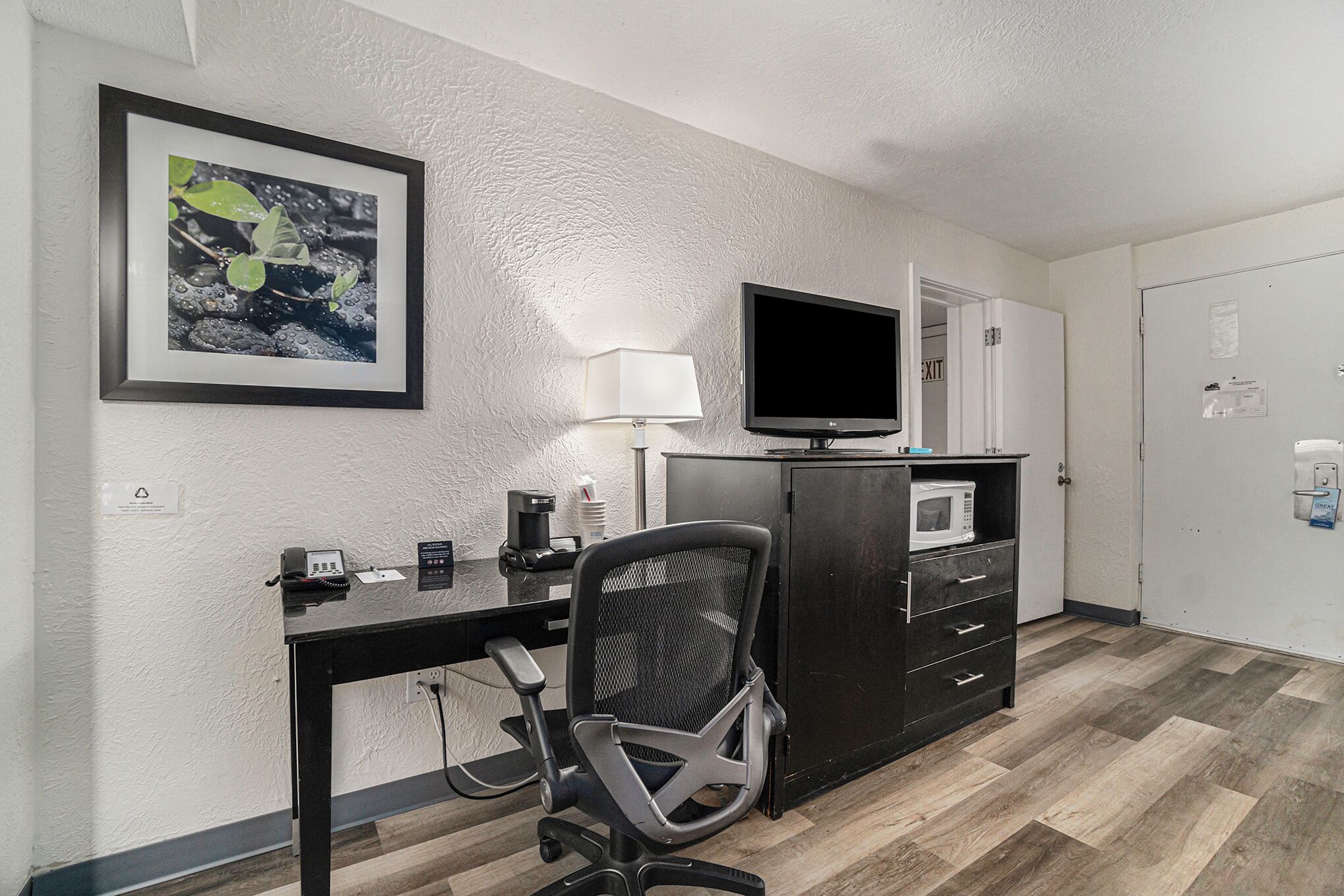 Ett hotellrum med ett skrivbord, en stol, en tv, en mikrovågsugn och ett skåp.