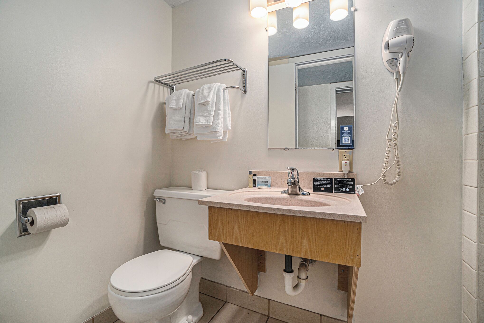 A bathroom with a toilet, sink, towel rack, and a hairdryer mounted on the wall.