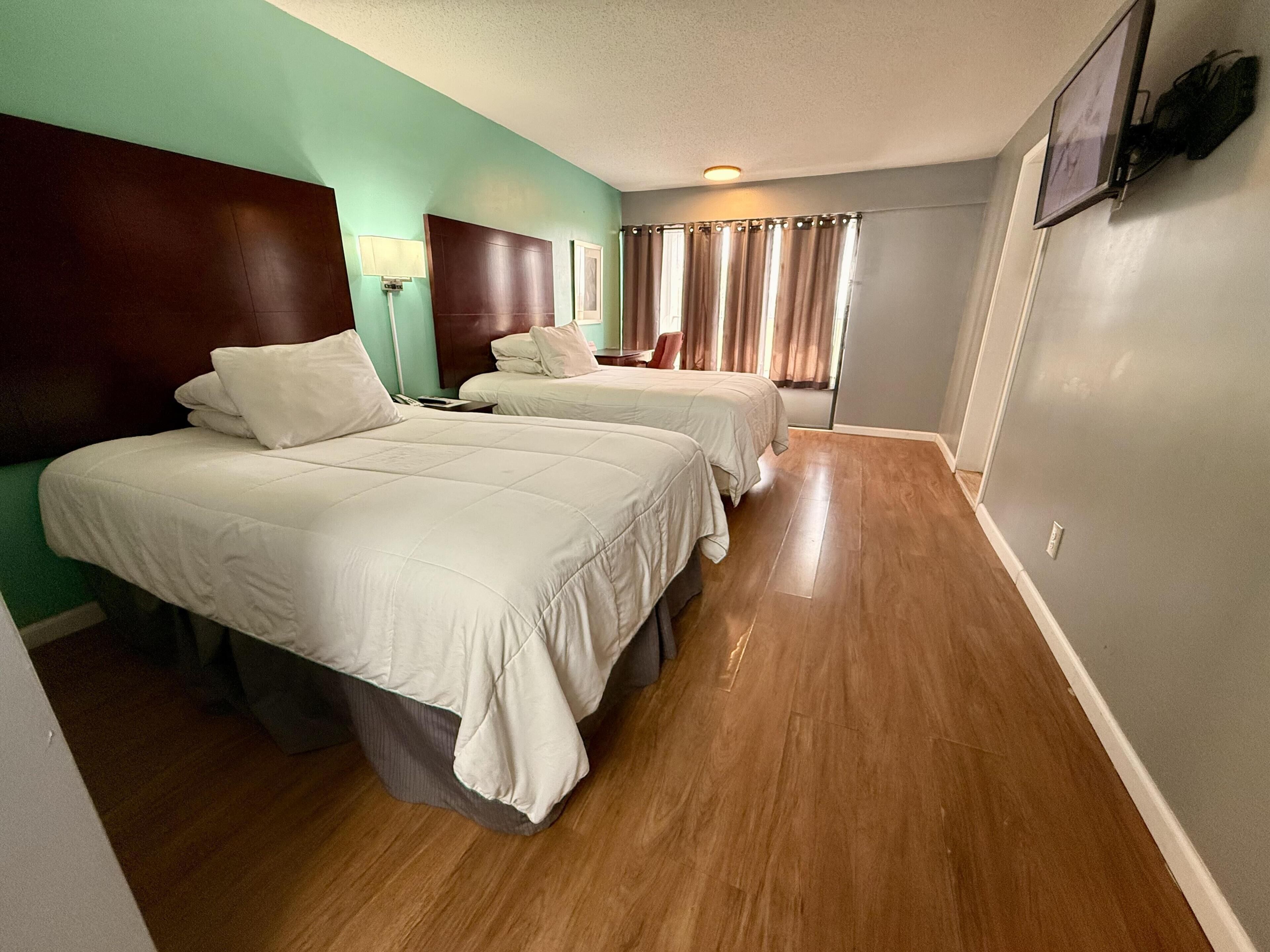 A hotel room with two beds, a wooden floor, a headboard, a lamp, and a TV mounted on the wall.