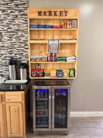 A kitchenette with a wooden shelf labeled 'MARKET' containing snacks and a sign with a menu.