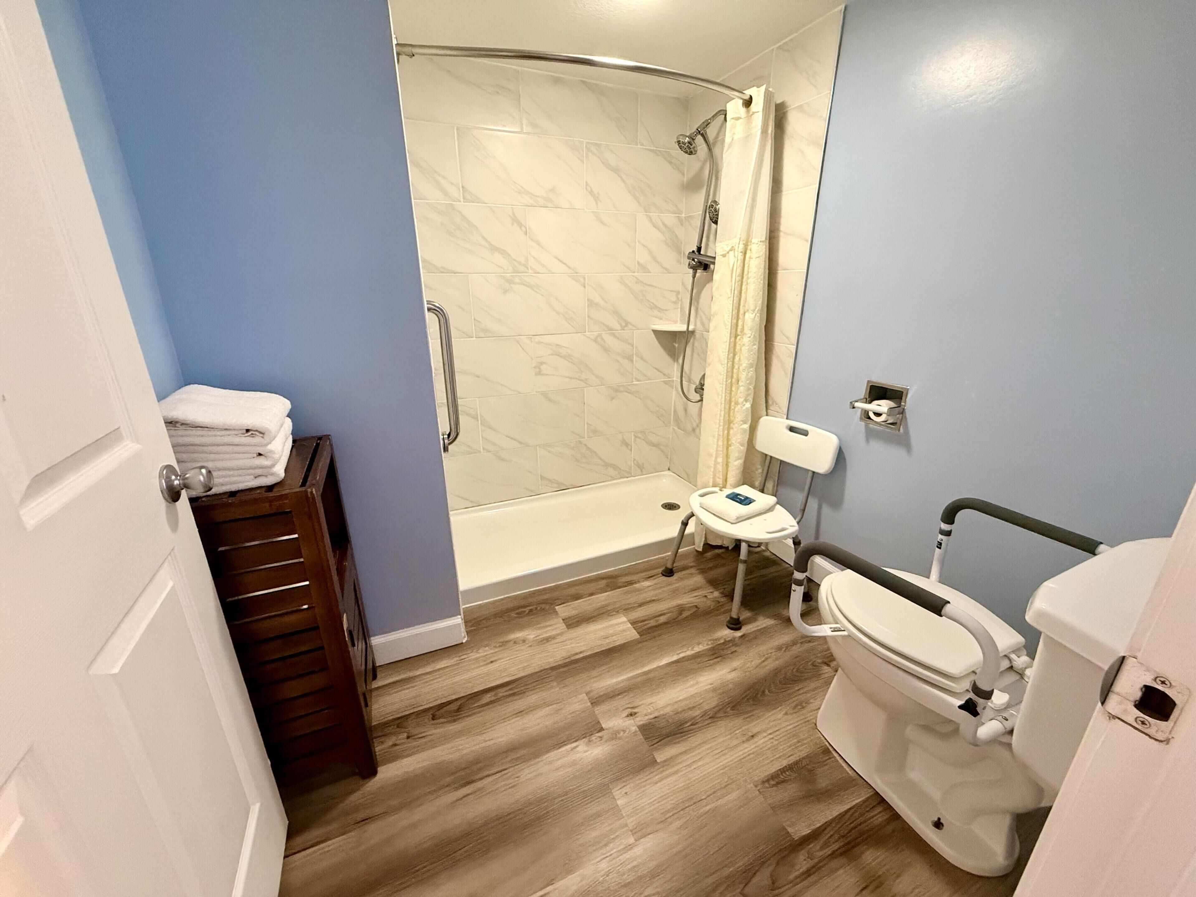 A bathroom with a shower, toilet, and a wheelchair-accessible chair.