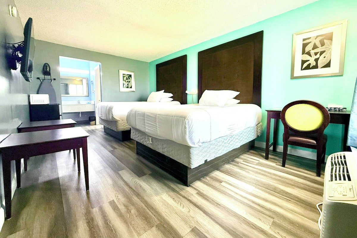A hotel room with two beds, a desk, a chair, a television, and a window.