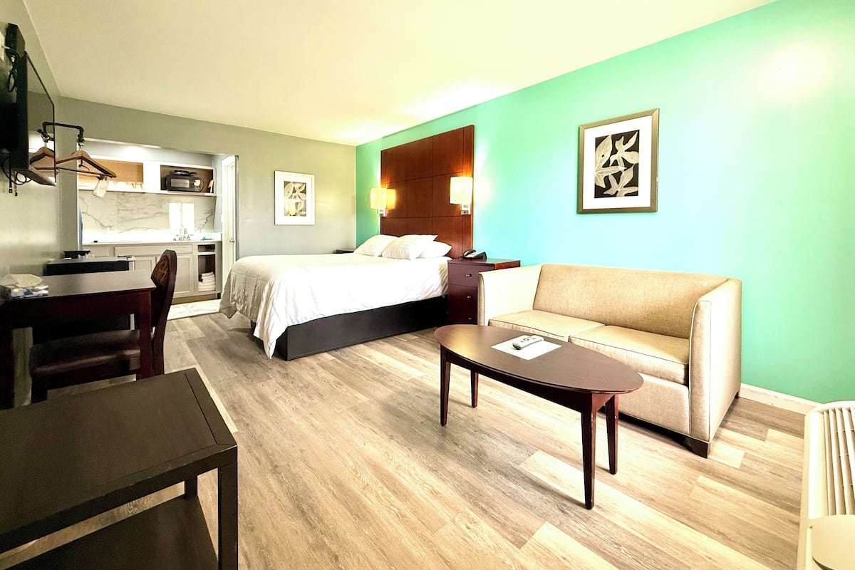 A hotel room with a bed, a sofa, a dining table, and a kitchen area.
