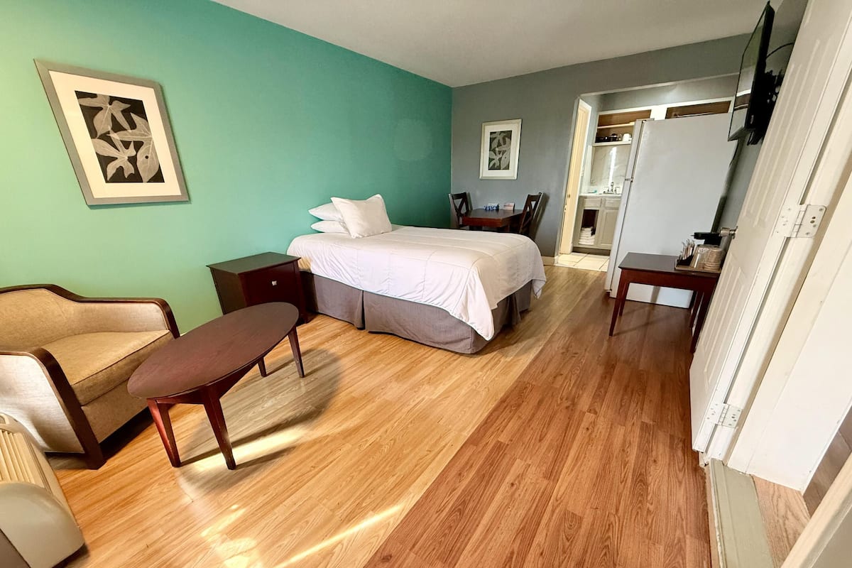 A bedroom with a bed, a chair, a bedside table, and a dresser.