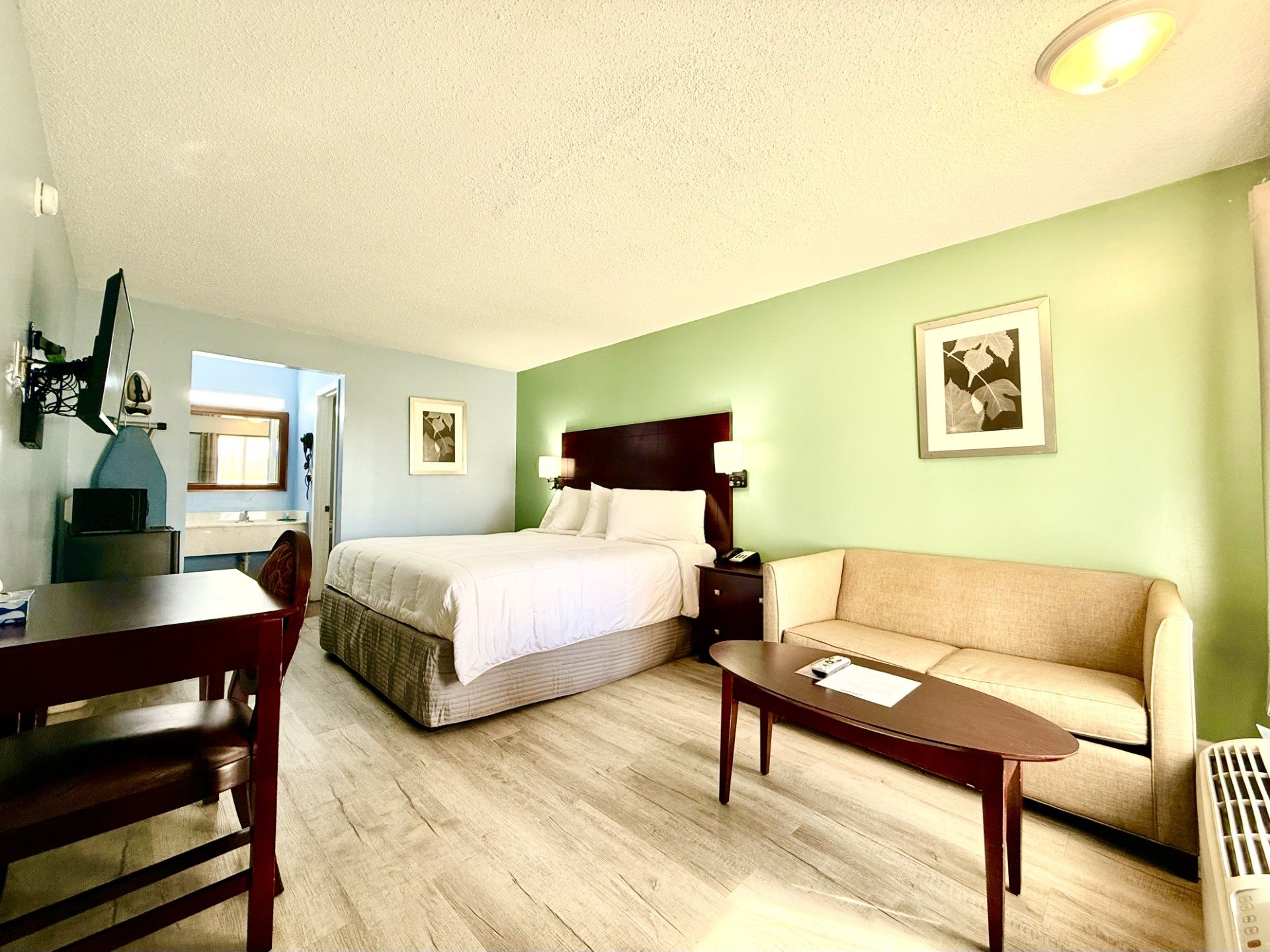 A hotel room with a bed, a sofa, a desk, and a chair. There is a window and a door visible.