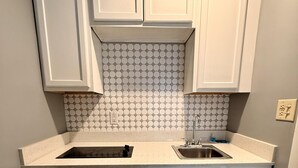 A kitchen with white cabinets, a tiled backsplash, and a stainless steel sink. - Americas Best Value Inn Suites & Studios Blytheville by Sonesta (Blytheville)