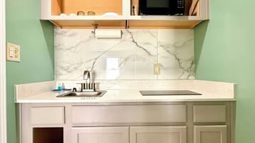 A kitchen with a marble backsplash, a microwave, and a sink.