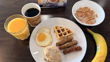 A breakfast plate with waffles, sausage, eggs, and a banana.