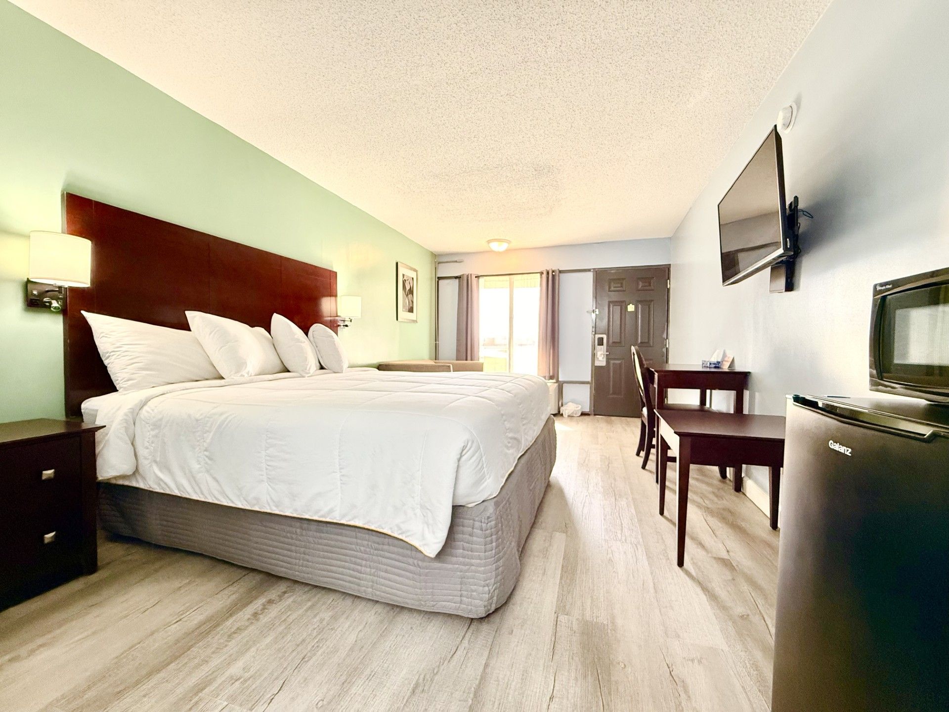 Habitación de hotel con cama, mesita de noche, lámpara, televisor y escritorio con silla.
