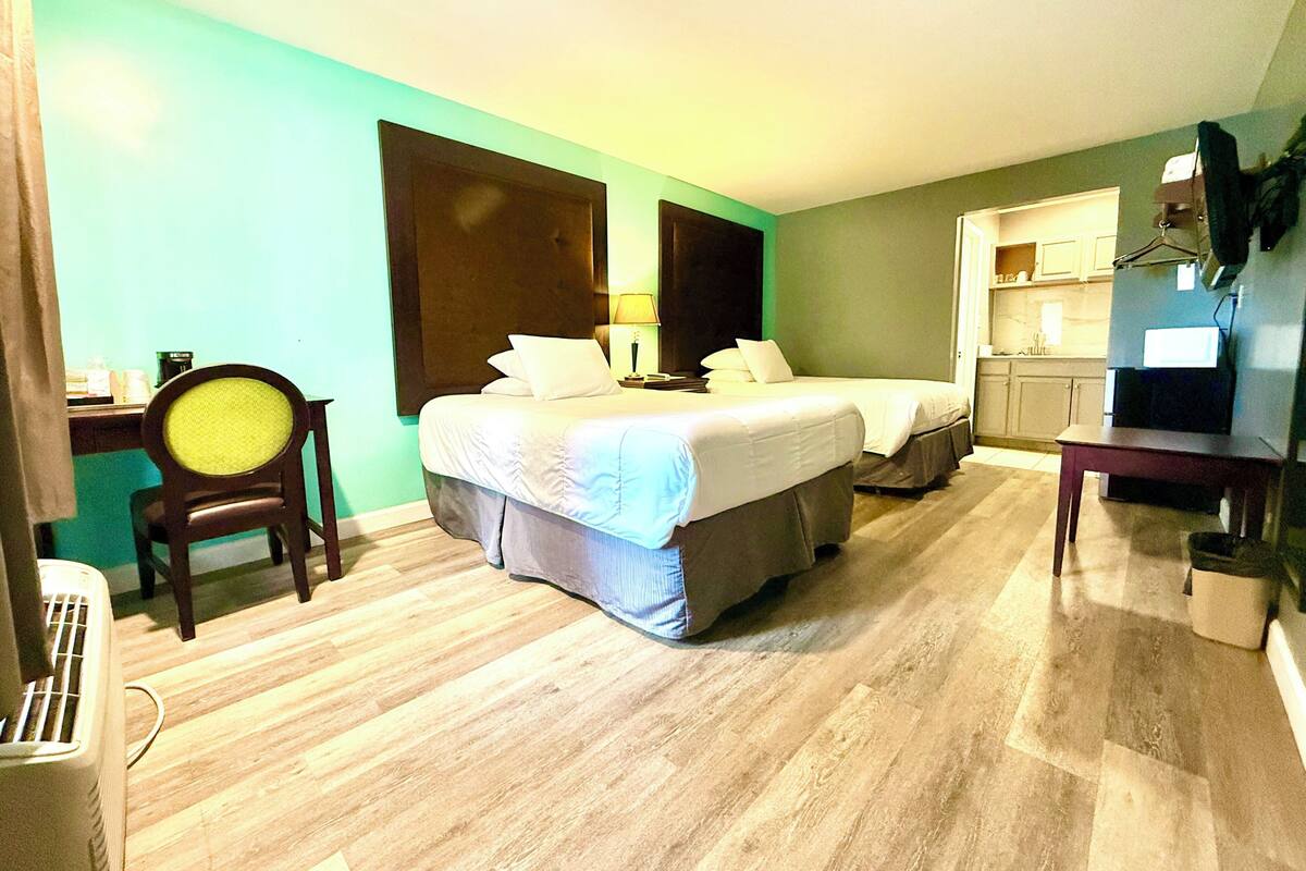 A hotel room with two beds, a desk, a chair, a TV, and a kitchenette.