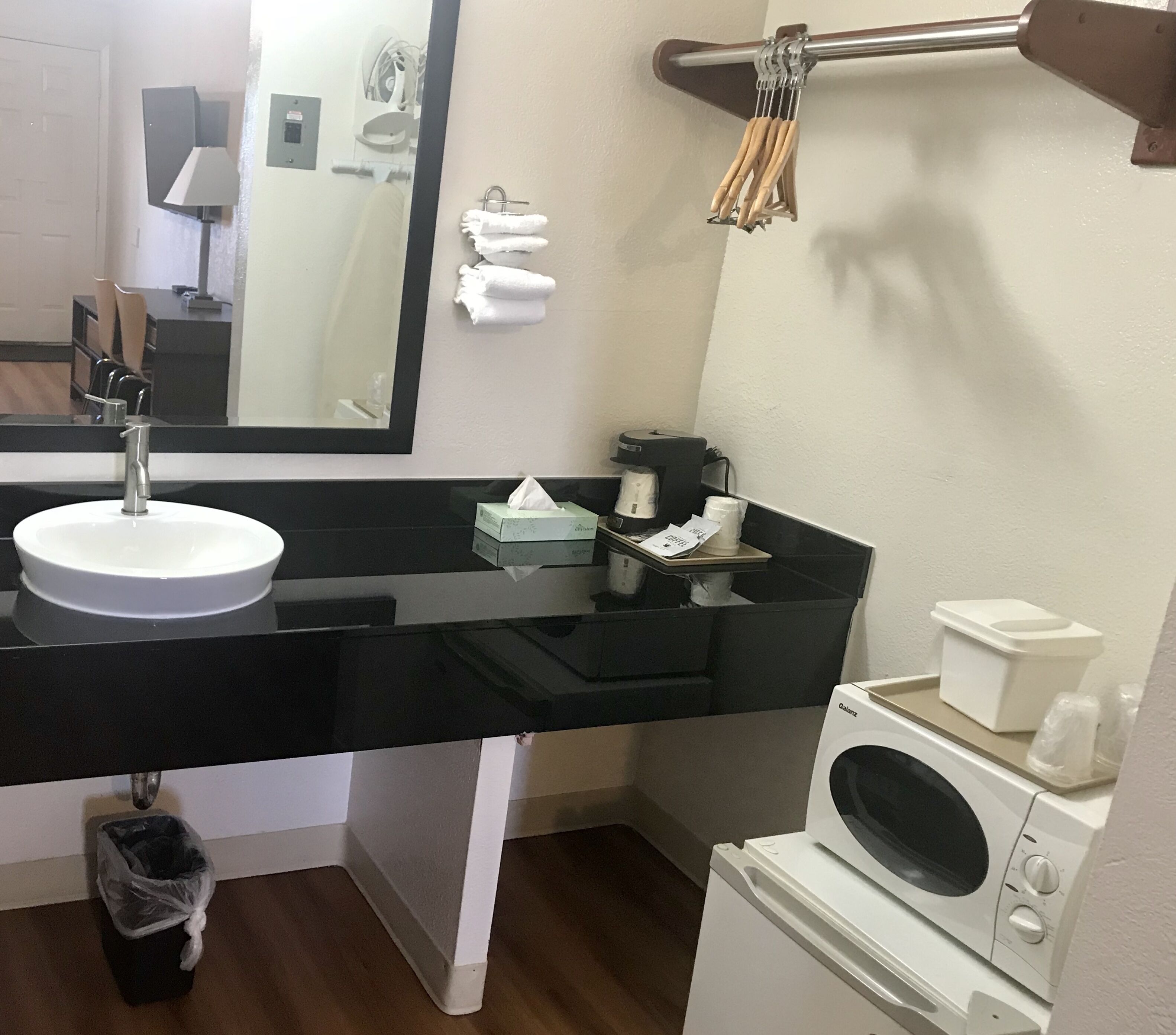 Casa de banho com lavatório branco, espelho, porta-toalhas, máquina de café e máquina de lavar roupa.