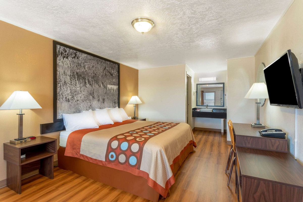Habitación de hotel con una cama grande, dos mesitas de noche con lámparas, un escritorio con una silla, un televisor de pantalla plana y una obra de arte grande en la pared.