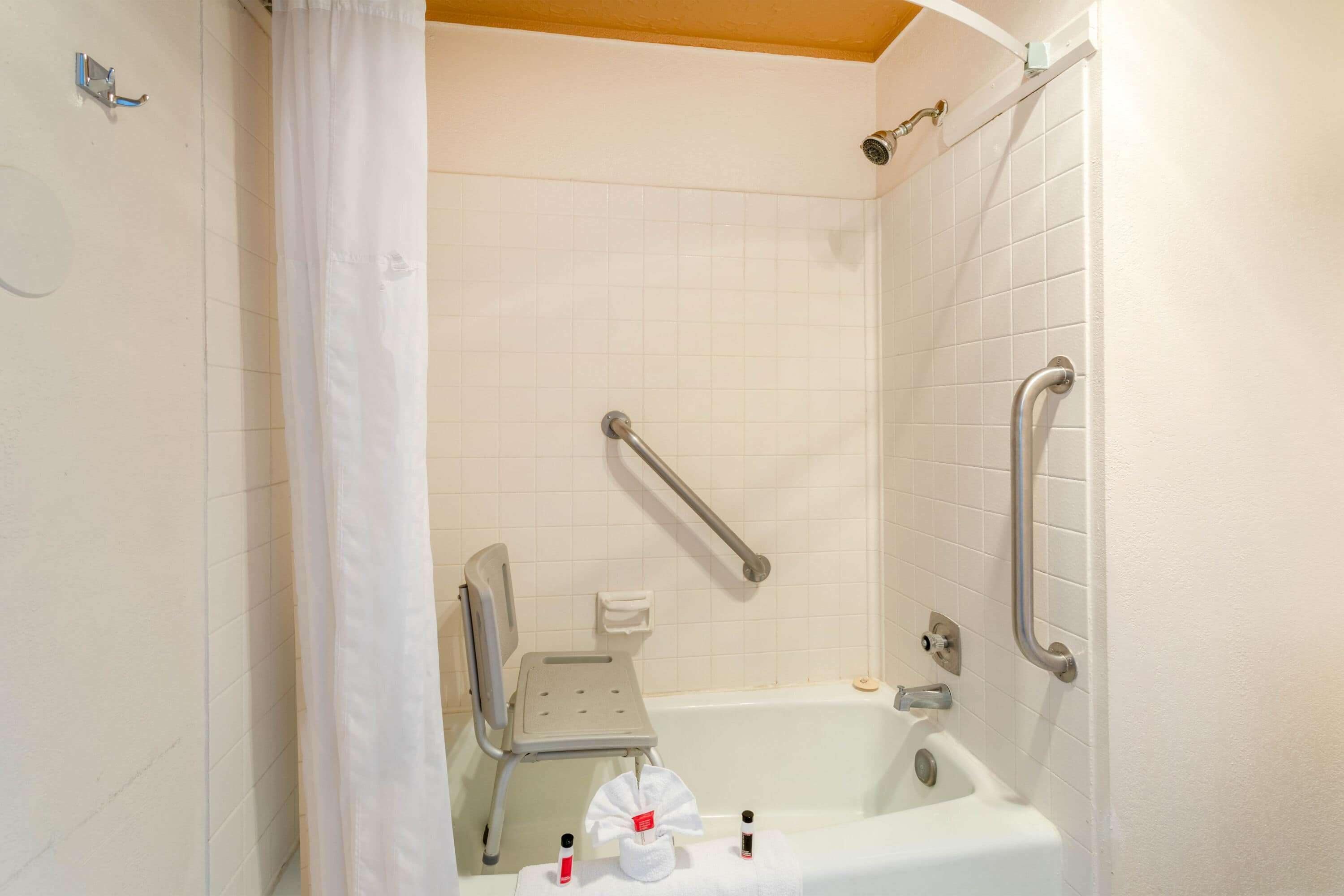 A bathroom with a white bathtub, grab bars, a shower chair, and a hand dryer.