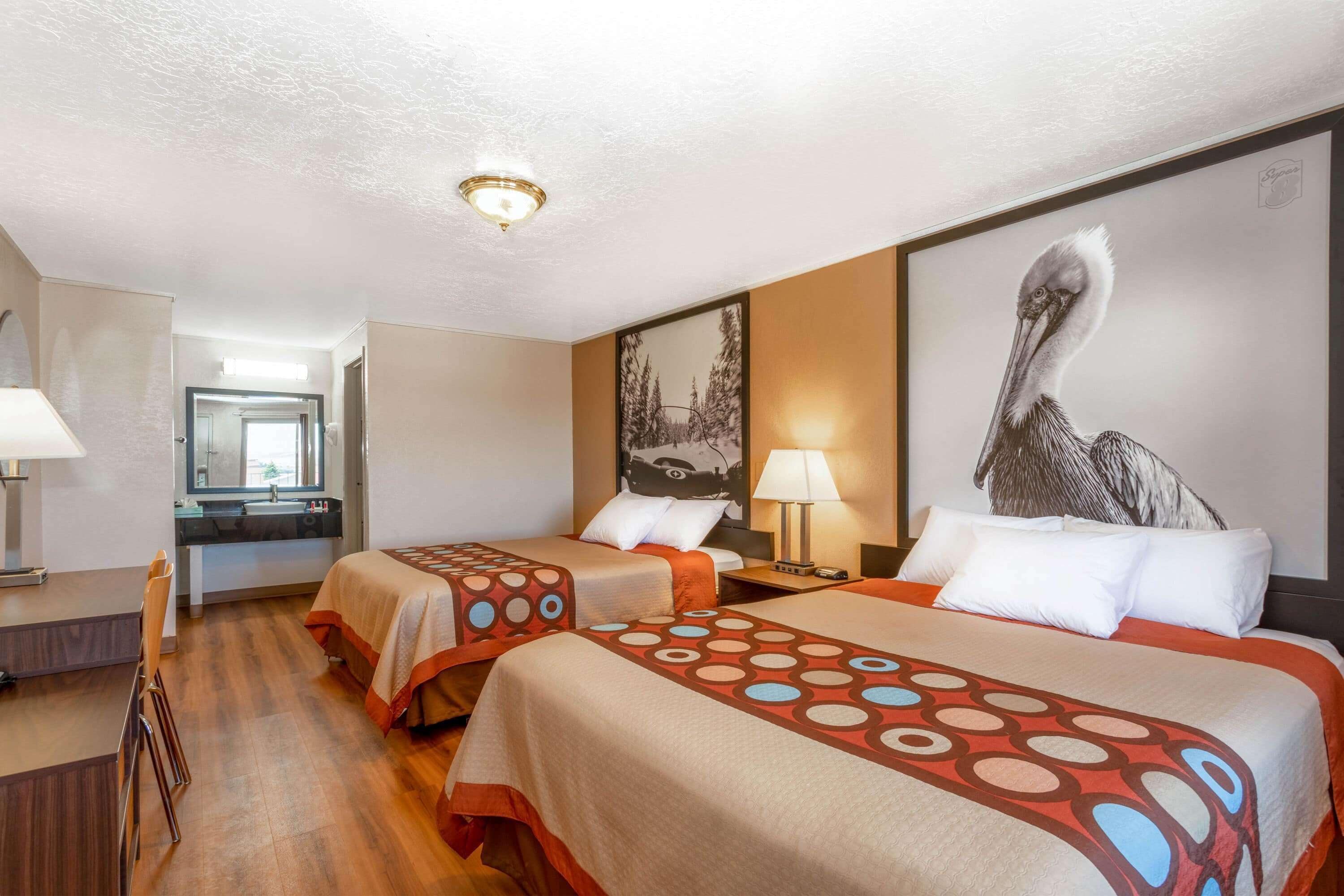 A hotel room with two beds, a desk, and a bathroom.
