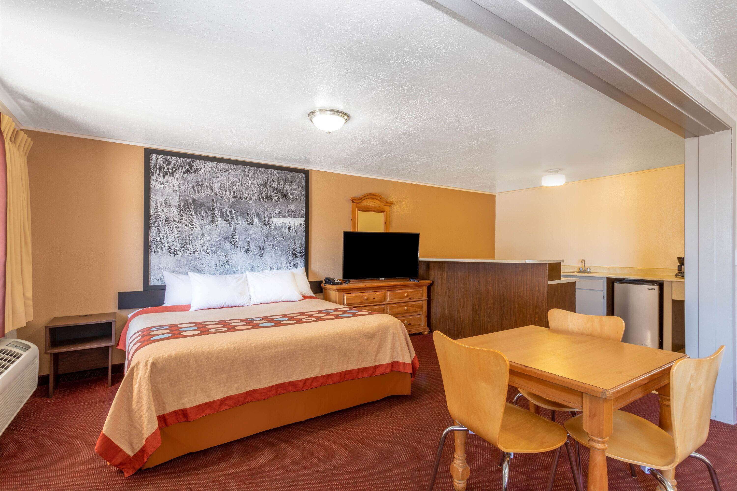 Une chambre d’hôtel comprenant un lit, un bureau, une chaise, une télévision, une petite kitchenette et un tableau au mur.