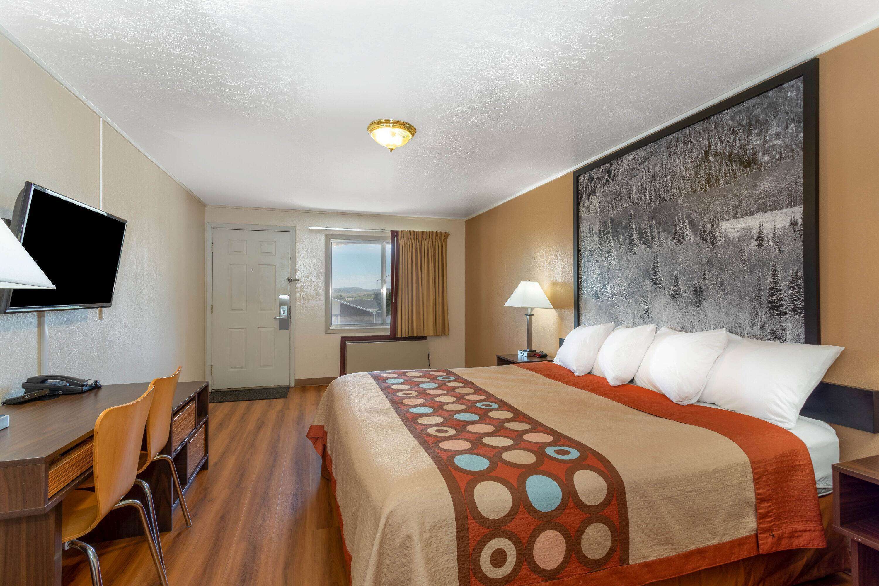 A hotel room with a large bed, a desk with a chair, a television, and a painting on the wall.