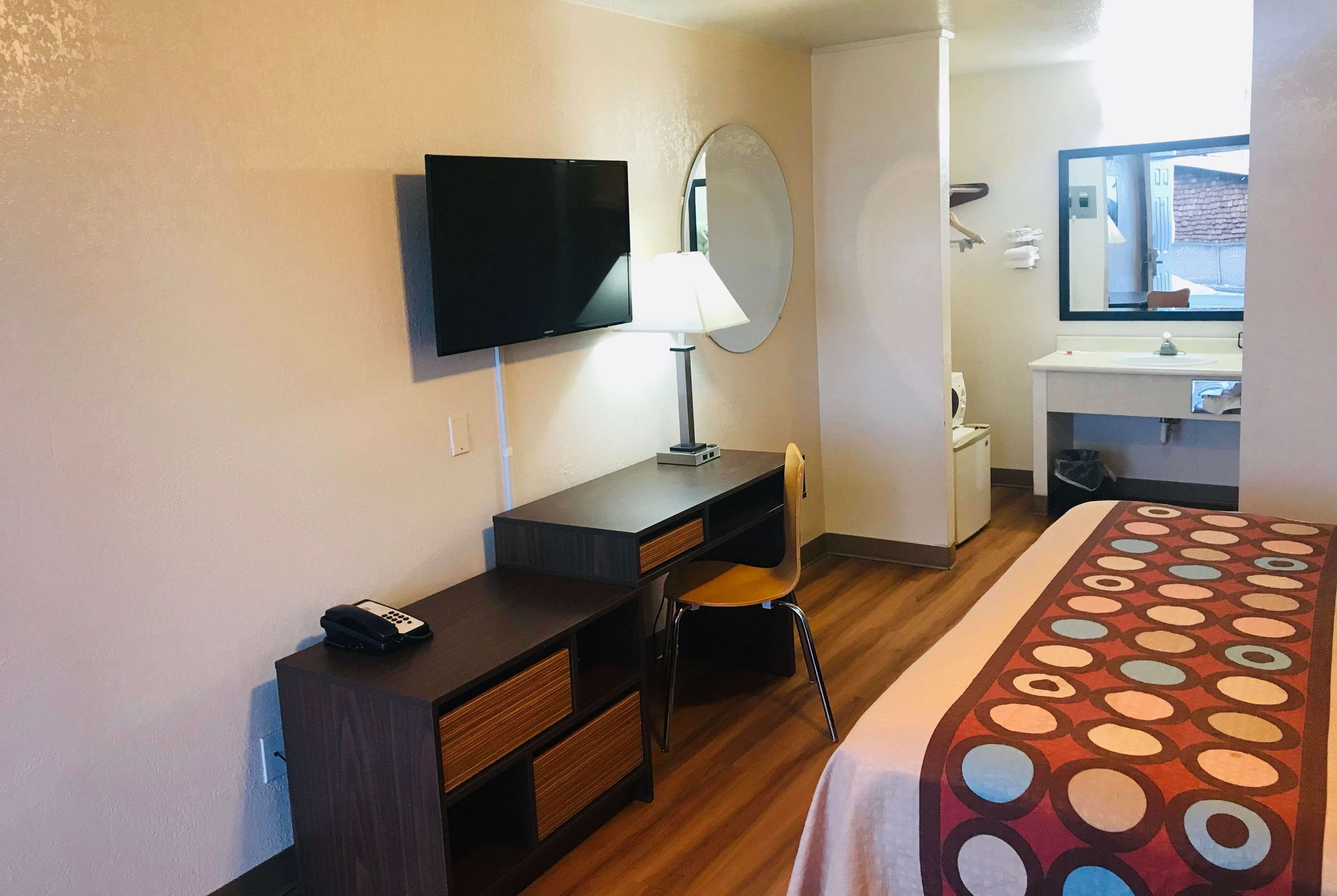 A hotel room with a bed, a desk with a chair, a television, a mirror, a sink, and a window.