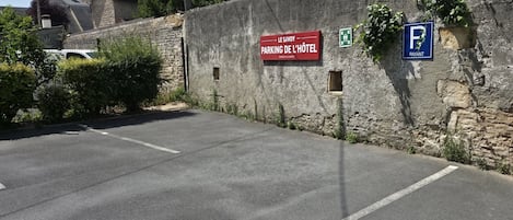 A parking area with a stone wall, a red sign indicating hotel parking, and a blue parking sign.
