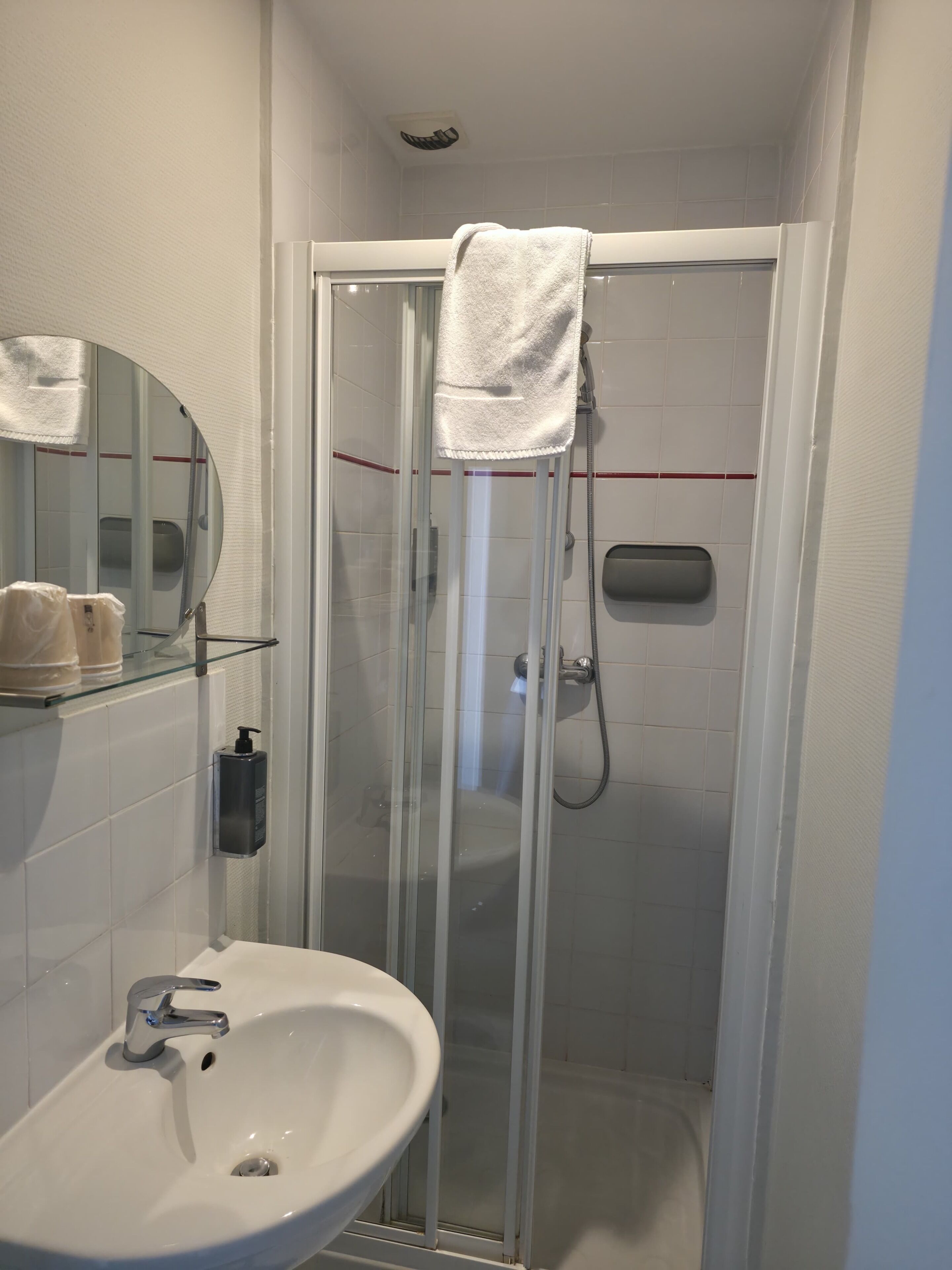 Une salle de bain avec une douche à parois de verre, un lavabo blanc et un miroir sur lequel est accrochée une serviette.