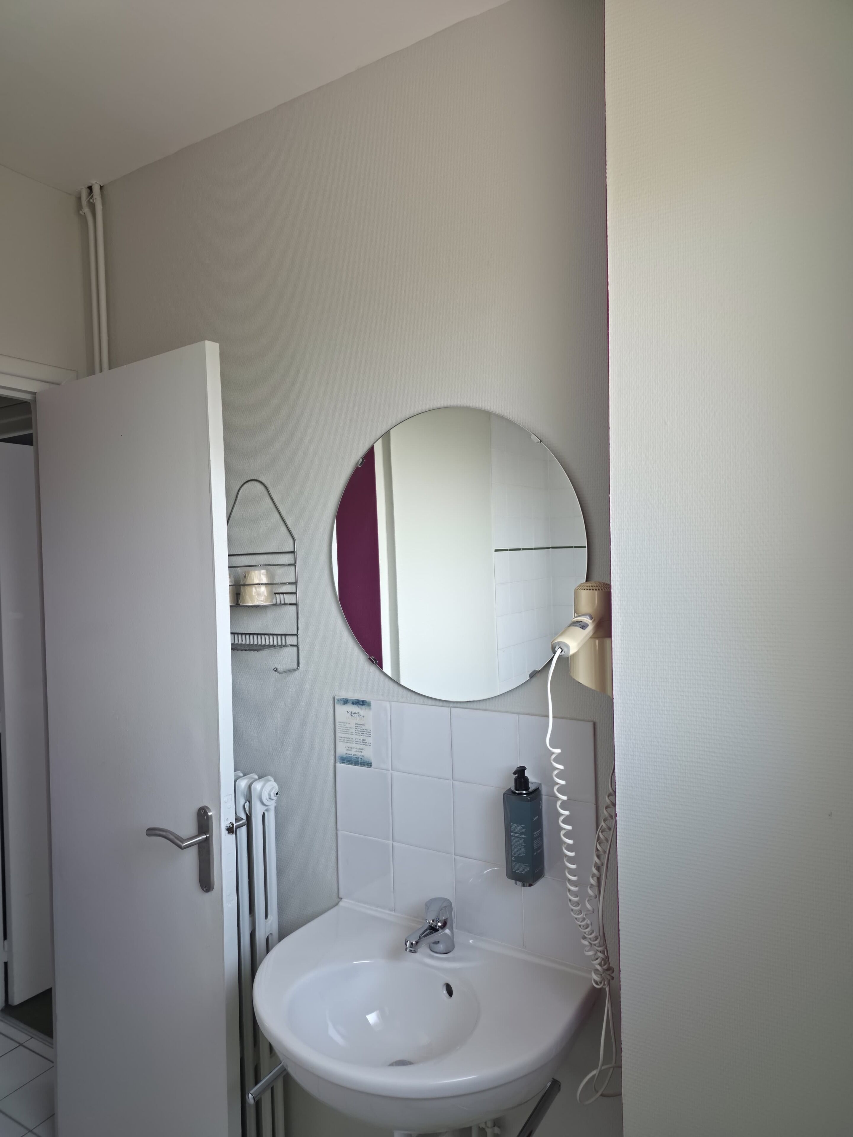 Un bagno con un lavandino bianco, uno specchio rotondo e un portasciugamani.