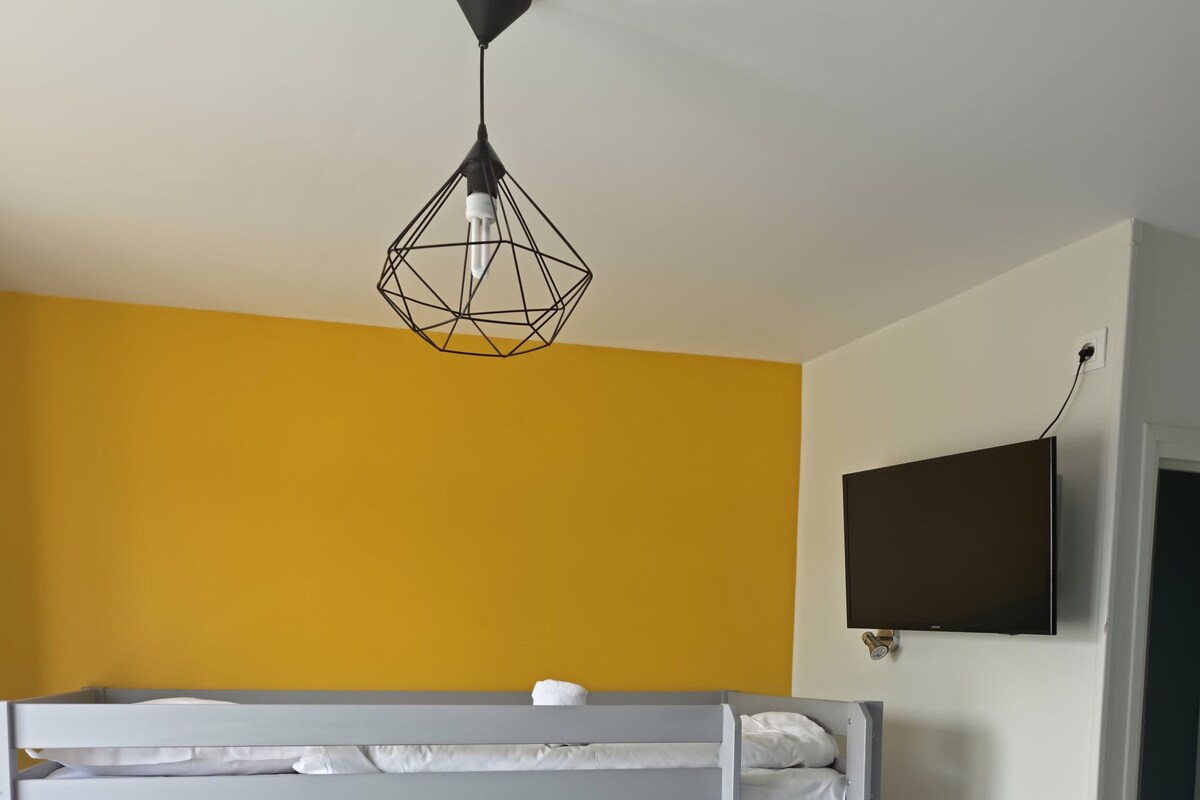 Habitación con literas, un televisor en la pared, una lámpara colgante y un par de toallas en el suelo.