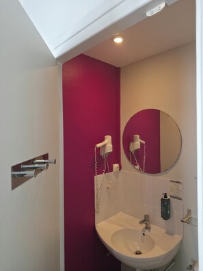 A bathroom with a white sink, a mirror, and a hairdryer mounted on the wall. - The Originals City, Hôtel Le Savoy, Caen (Caen)