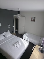 Habitación de hotel con dos camas, cafetera, una mesita y puerta que da a un baño.
