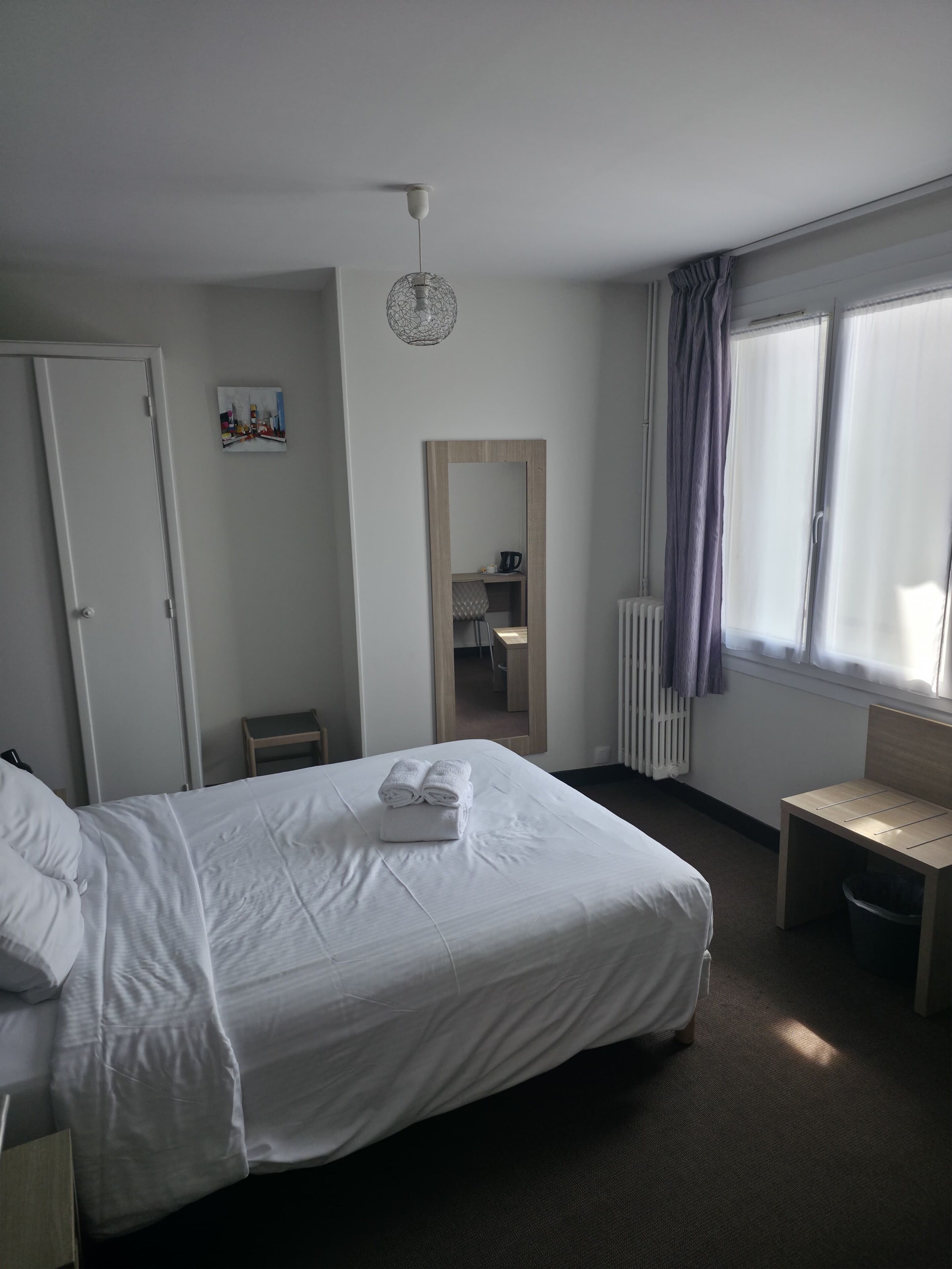 Habitación de hotel con cama, una silla, un escritorio, un radiador y una ventana con cortinas.