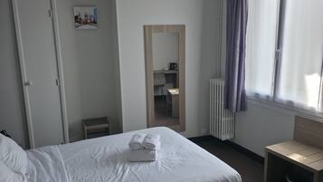 Una camera d'albergo con un letto, una sedia, una scrivania, un termosifone e una finestra con tende.