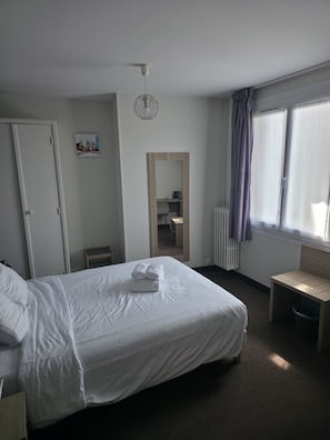 Une chambre d’hôtel avec un lit, une chaise, un bureau, un radiateur et une fenêtre avec des rideaux.