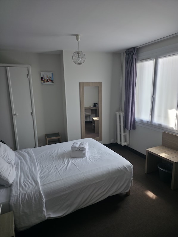 Habitación de hotel con cama, una silla, un escritorio, un radiador y una ventana con cortinas.