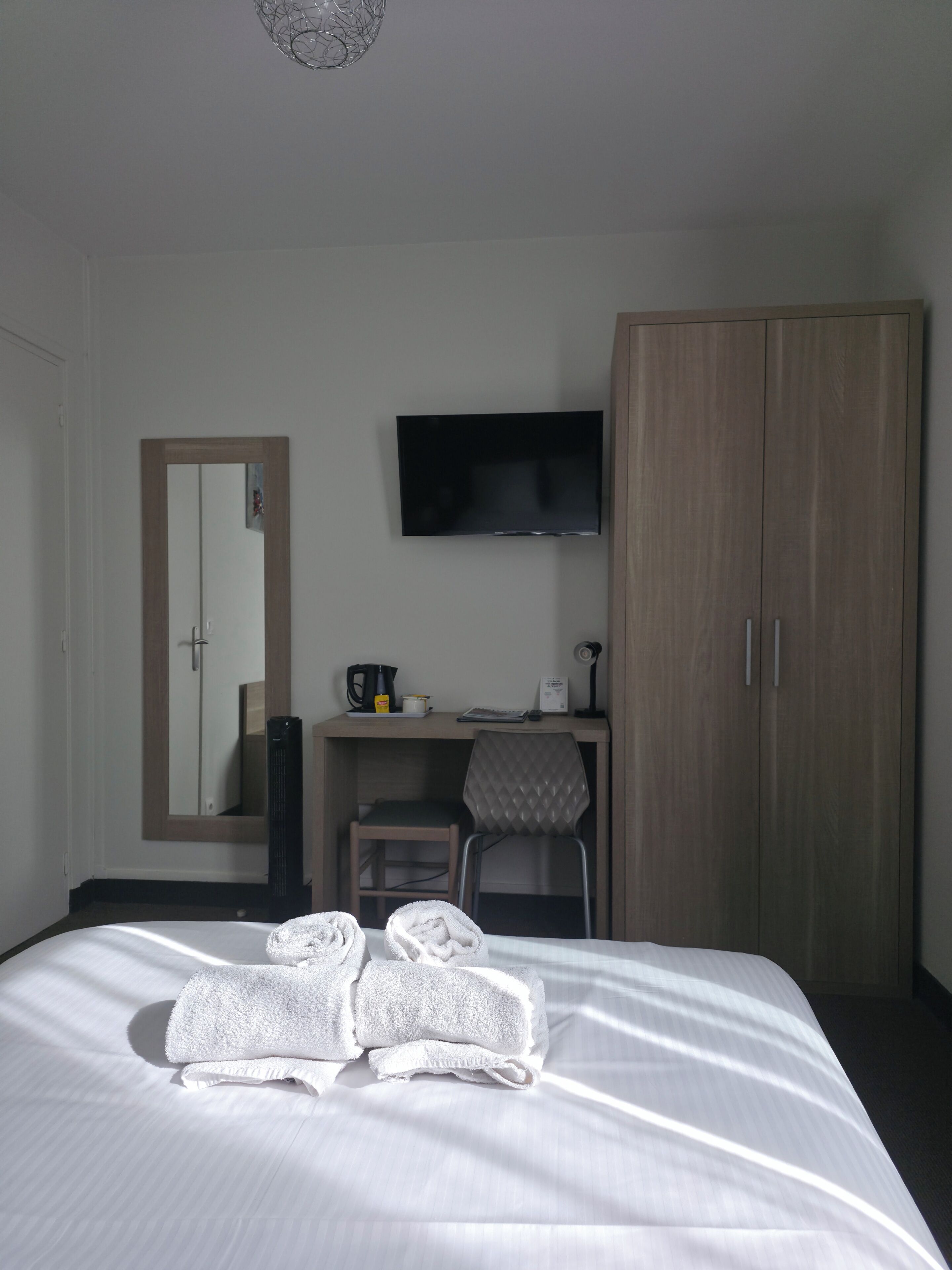 A hotel room with a bed, a desk, a television, and a wardrobe.