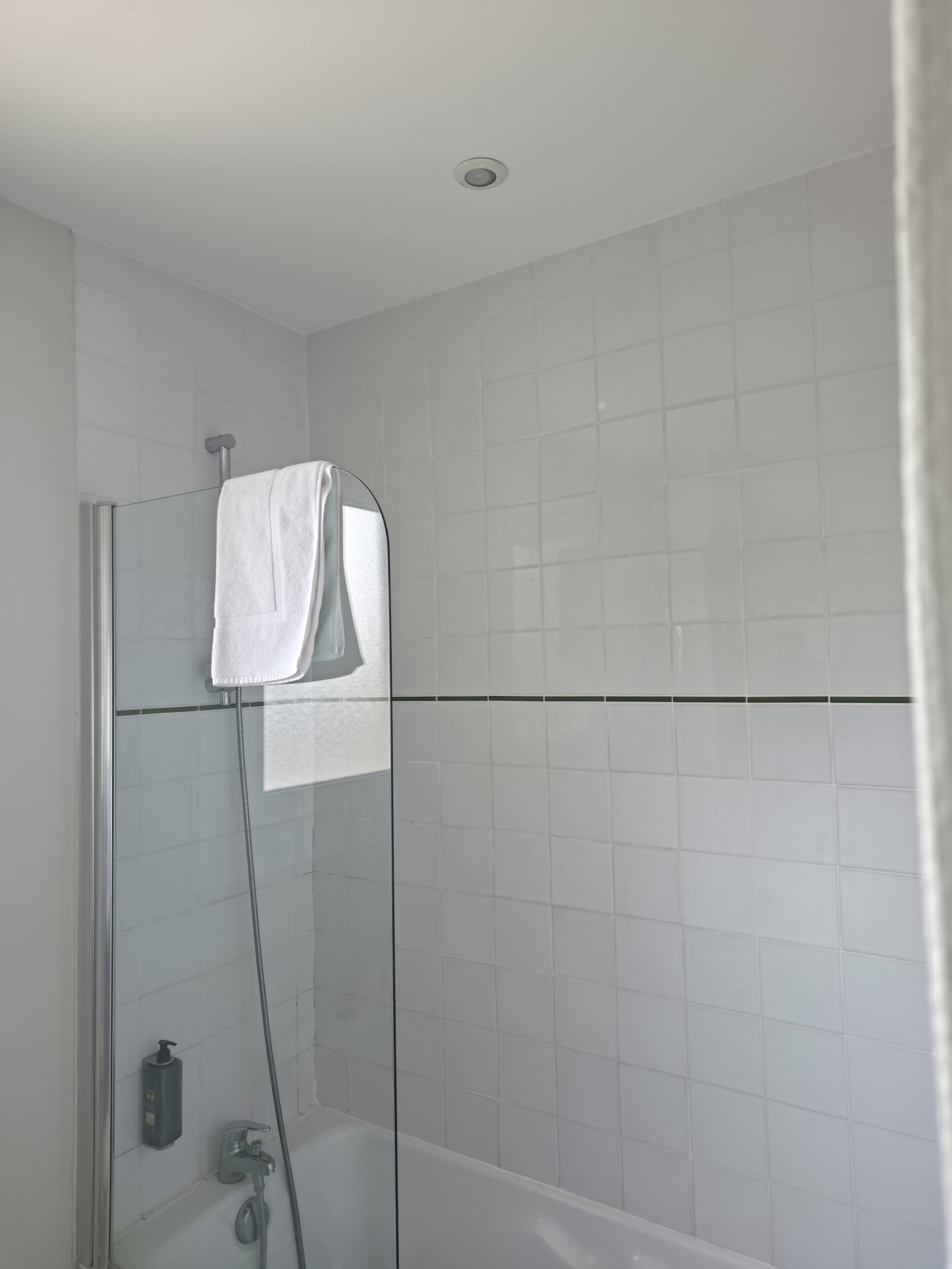 Een moderne badkamer met een douchecabine van glas, een wit bad en een handdoek aan de douchedeur.
