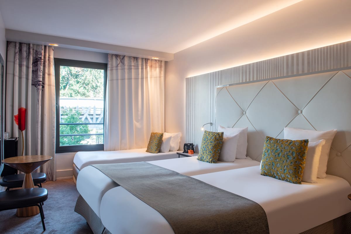 A hotel room with two beds, a desk, and a chair.