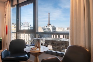 A room with a view of the Eiffel Tower, a table with a bottle and glasses, and two chairs. - Le Parisis Paris Tour Eiffel (Paris)