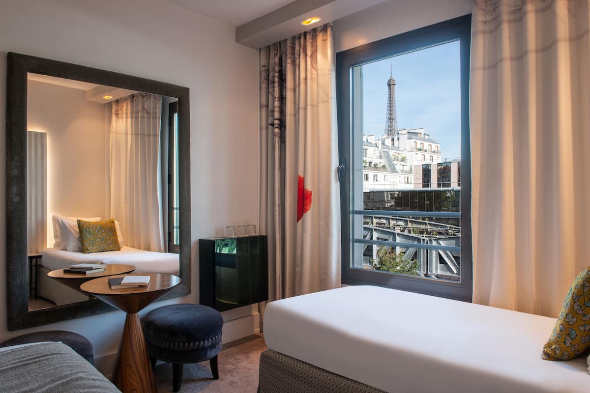 A hotel room with a bed, a desk, a chair, a TV, and a large window with a view of a bridge and buildings.
