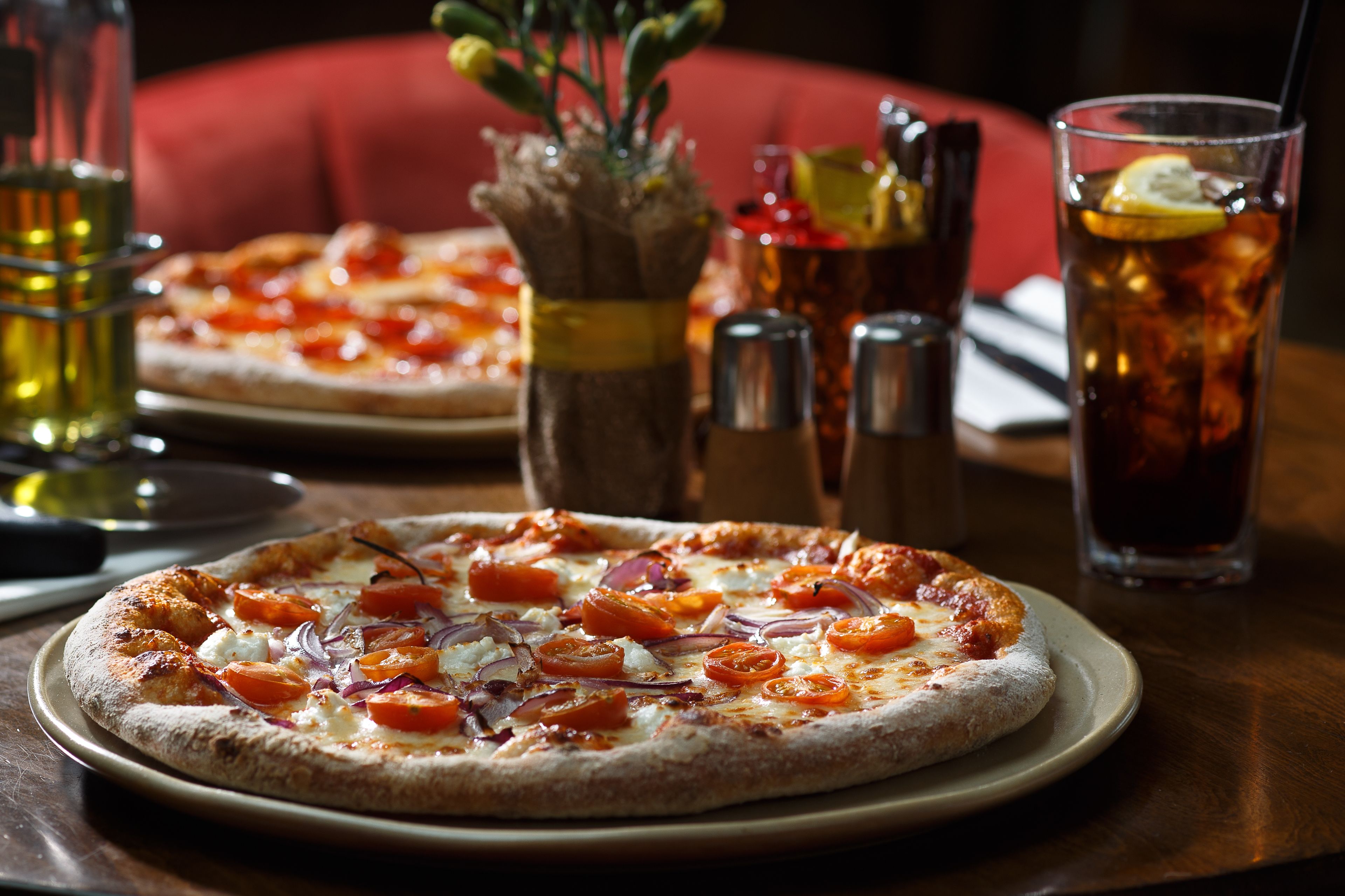 A pizza with toppings on a plate, a glass of iced tea, and condiments on a table.
