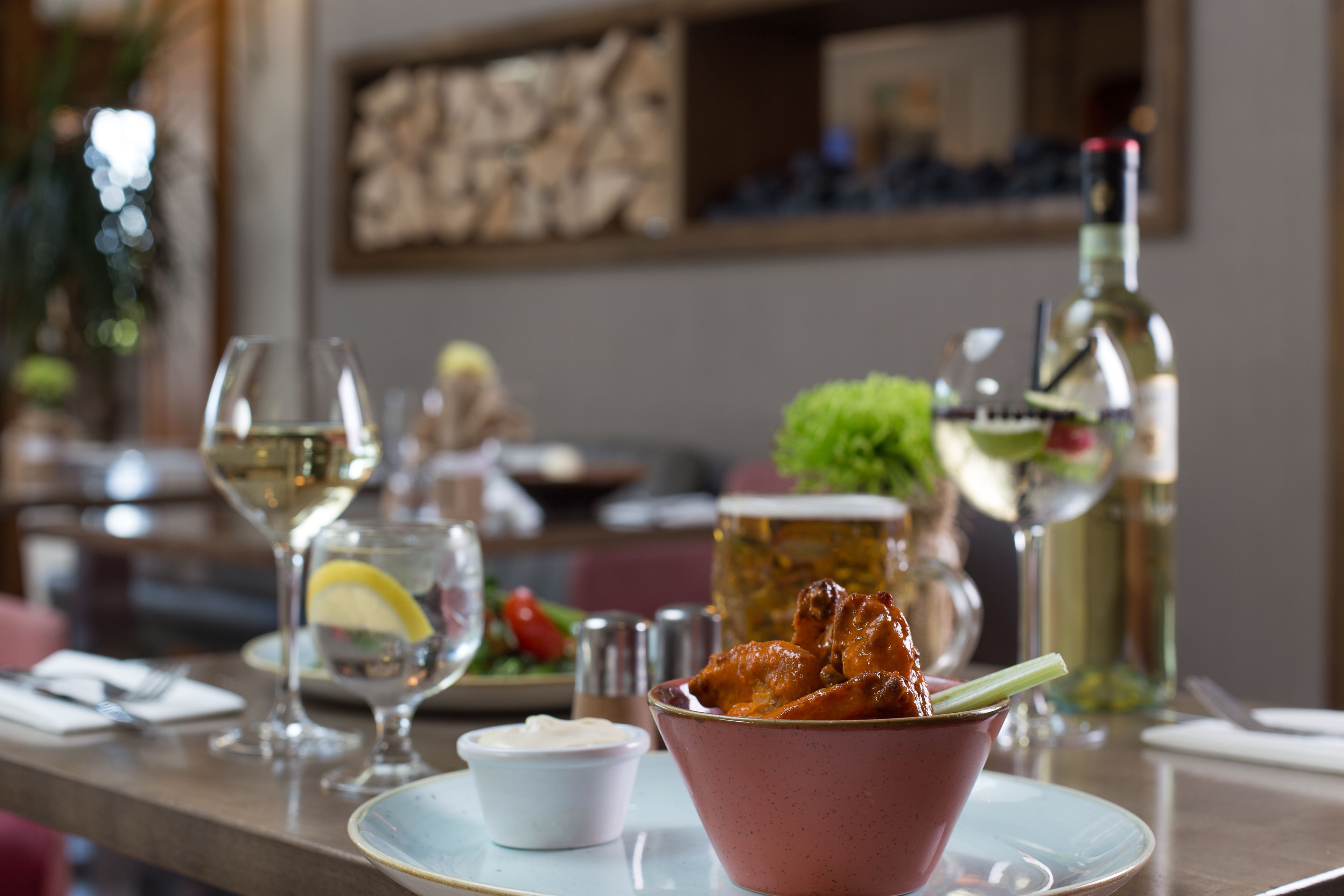 A dining table with a bowl of food, a glass of white wine, and a bottle of olive oil.