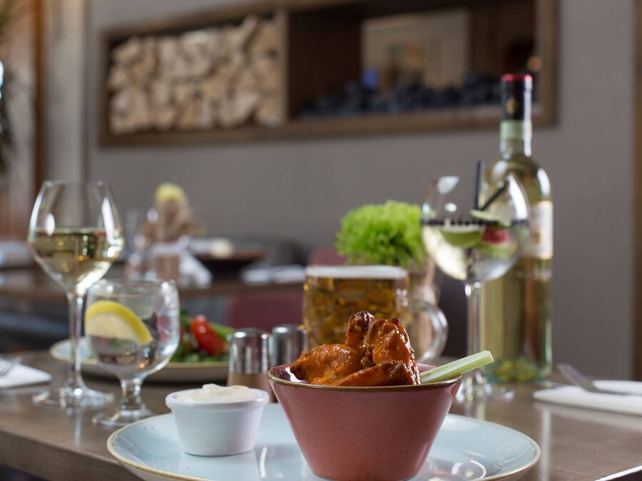 A dining table with a bowl of food, a glass of white wine, and a bottle of olive oil.